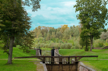 Fototapeta premium Old gateway on the channel. Wooden dam on the river. Autumn landscape.