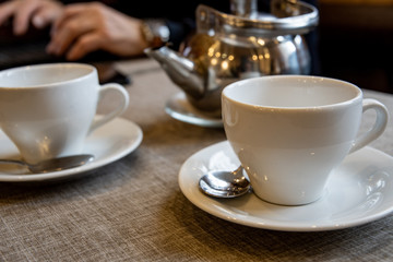 A metal teapot for tea brewing, a white ceramic cup, a glass vase for sugar on a table in a cafe.