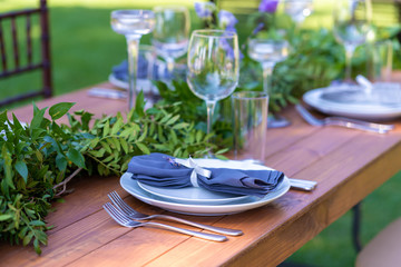 Beautifully decorated wooden table in a summer open-air cafe. Green branch and fresh flowers table decoration