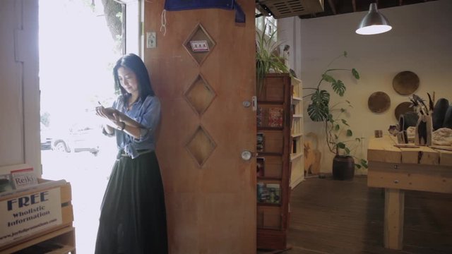 Female shop owner using digital tablet in bookshop doorway