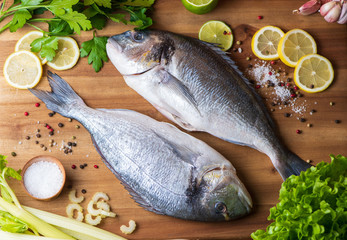 fresh fish with lemon, salt and pepper on wooden board