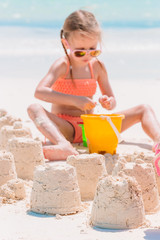 Little girl at tropical white beach making sand castle