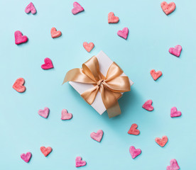 Close up of gift box with golden tied bow, among heart shapes. Top view holiday background.