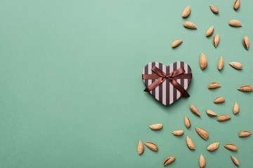 Heart shaped gift box among scattered almond with copy space to the left. View from above.