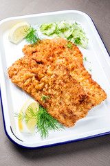 Traditional deep fried Wiener schnitzel from veal topside with cucumber salad and cranberry jam offered as closeup on a white tray