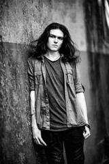 Fototapeta premium a black-and-white photo of a young man with long, dark hair and brown eyes, a face with freckles, walking down the street in a stylish shirt and jeans,in a Cagle style, in a sad mood