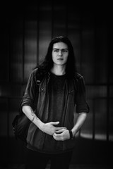 a black-and-white photo of a young man with long, dark hair and brown eyes, a face with freckles, walking down the street in a stylish shirt and jeans,in a Cagle style, in a sad mood