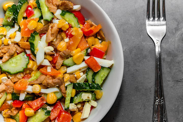 Bright vegetable salad with chicken on a gray concrete background. Making a delicious salad for a healthy diet.