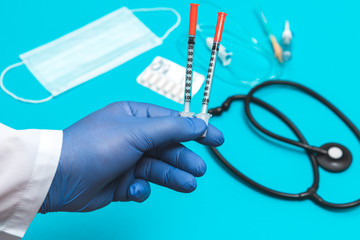 doctor's hand in a white coat and blue sterilized surgical glove holding two empty insulin syringes, blurred background with medical tools