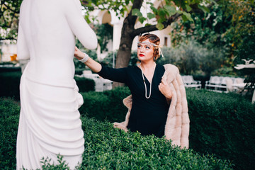 a gorgeous woman in a fur cape and a diadem on her head walks through her garden surrounded by...