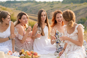 The company of gorgeous female friends having fun, drink wine, and enjoy hills landscape picnic