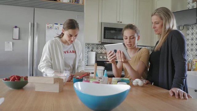 Mother and daughters with digital tablet baking in kitchen