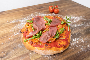 homemade pizza margherita with tomato sauce, mozzarella, served on a floured wooden table decorated with fresh tomatoes