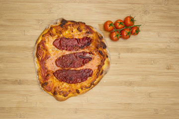 perfectly baked homemade pizza with tomato sauce, mozzarella and beef ham on a wooden table decorated with fresh tomatoes