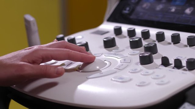 Close-up of obstertician's hand using control panel of ultrasound machine to fix fetal parameters during prenatal test. Gynecologist adjusting image of fetus during pregnancy ultrasound in clinic