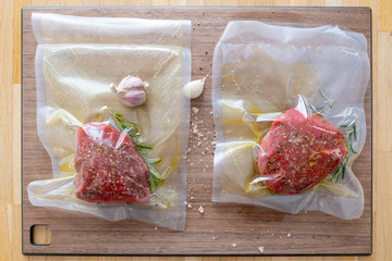 Marinated sous vide steak in a vacuum bag with olive oil and rosemary on a wooden cutting board