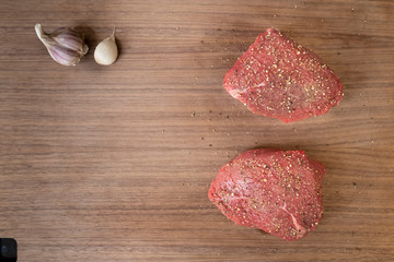 two raw peppered beef steak on dark wooden cutting board with garlic