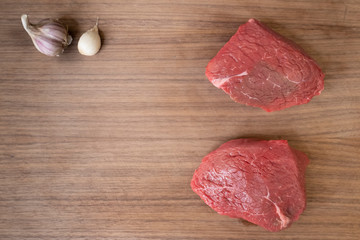 two raw beef steak on dark wooden cutting board with garlic