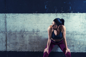 Fitness woman in sports clothes leaning on concrete background and looking aside. Copy space. Training and sport.