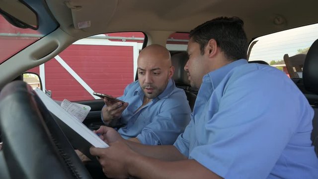 Event delivery men using smart phone and reviewing paperwork inside truck