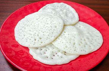 Kerala Special Appams in a red plate on a wooden table ready to be eaten.