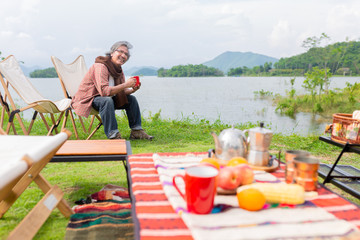 asian senior man travel in forest, he drinking hot coffee at lakeside , happiness retirement activity, adventure and travel
