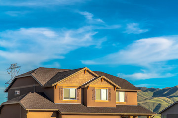 House exterior with dormers and gray roof against hills and cloudy blue sky