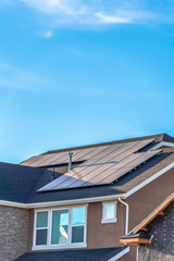Gray roof of home with solar panels and pipe vents against blue sky background