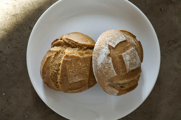 Two soft fresh baked white bread with a crispy crust on a white plate on textured table