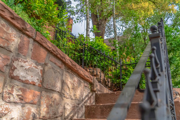Close up of outdoor stairs with black metal handrail against a stone wall
