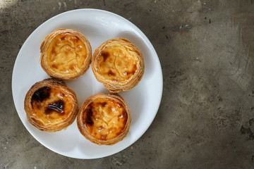 Four portuguese pasteis of cake with custard on white plate on textured background