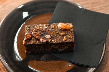 A delicious brown cake with nuts on a black plate with a black napkin on the table