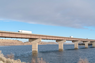 Fototapeta na wymiar Huge trucks travelling on a massive bridge against snowy hills and cloudy sky
