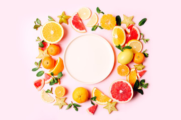Fresh citrus fruits around the plate on pink background. Copy space. Mock up