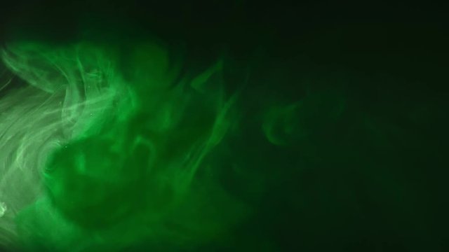 Green paint drops mixing in water slow motion. Smooth ink swirling and splashing from above underwater. Ink cloud on black background. Colored abstract smoke explosion.