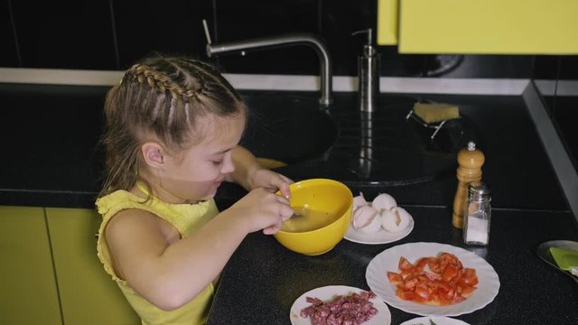Smart girl learning to cook. Happy and serious young mistress children to cook a Neapolitan egg fried omelette from sausage. Modern Built In Kitchen Appliances in green black color.