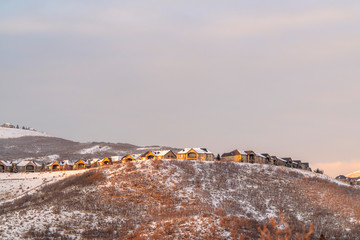 Neighborhood homes on top of snowy hills against cloudy sky at sunset
