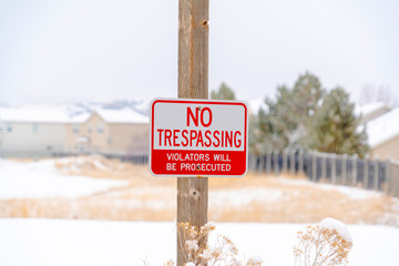 Fototapeta premium No Trespassing sign on wooden post against blurry snowy property in winter