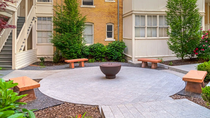 Panorama frame Stone benches around a fire pit outside a residential building on a sunny day