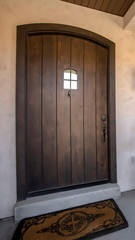 Vertical frame Brown wood arched front door with glass panes at the facade of home with porch