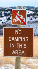 Vertical frame No Camping In This Area sign against a grassy landscape blanketed with snow