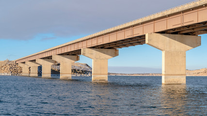 Panorama Stringer bridge spanning over a lake with view of snowy terrain and cloudy sky