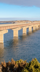 Fototapeta premium Vertical frame Blue lake with bridge connecting vast terrains blanketed with snow in winter