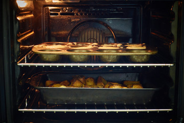 View through oven window of cooking roast potatoes and Yorkshire puddings                  