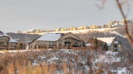Fototapeta na wymiar Photo Panorama frame Homes with snowy roofs on top of frosted hills against cloudy sky in winter