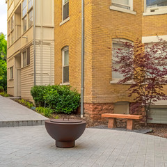 Square Fire pit on circular patio outside building with white and stone brick wall