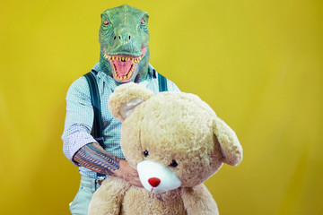 Senior man wearing t-rex dinosaur mask with teddy bear. Crazy man having fun celebrating carnival...