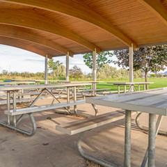 Square Eating area at a park with tables and seats under brown wood roof of pavilion