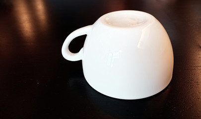 A white coffee cup upside down on a drak brown wood background