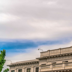 Fototapeta premium Square Building with white wall balcony and security camera on roof against cloudy sky
